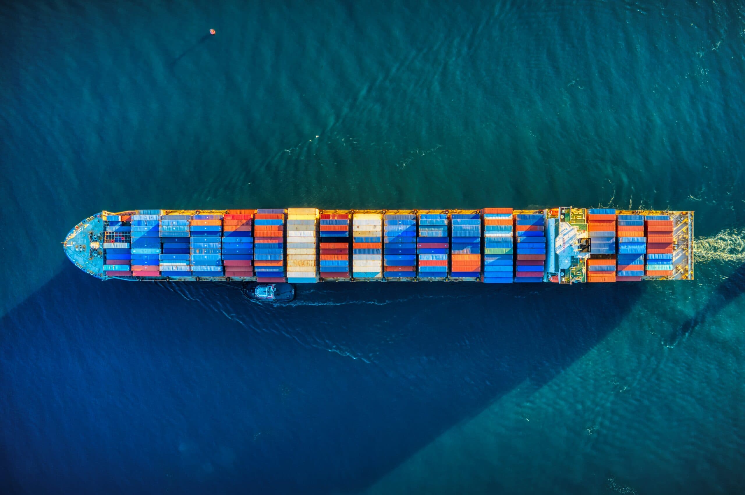 Loaded container ship under way with a tug alongside, aerial view